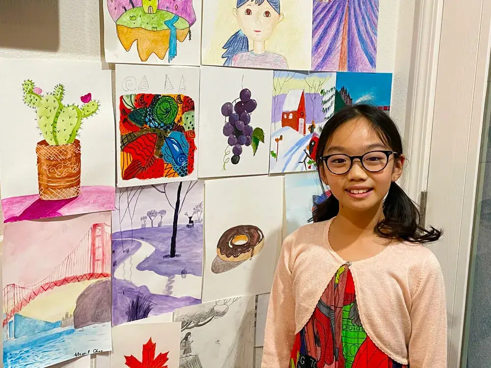 Abigail with a wall art of all her artworks completed at the online classes by Nimmy's Art located in Katy, Texas