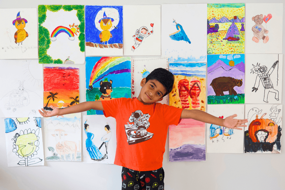 George standing proudly in front of a wall displaying his colorful paintings, featuring abstract and nature-inspired designs.