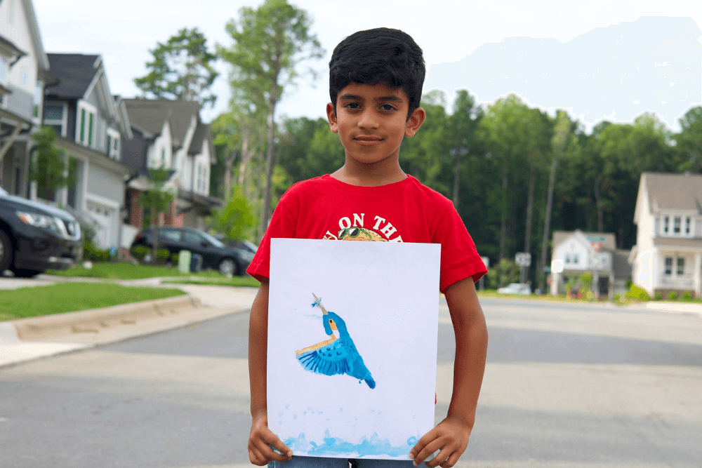 Young artist George proudly holds his vibrant kingfisher painting, showcasing bold colors and intricate details.