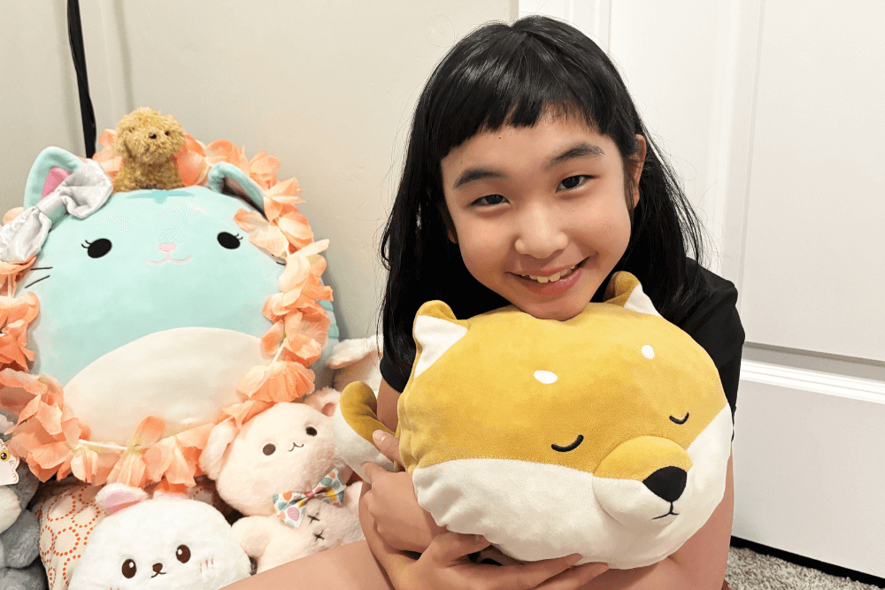 Bella, a cheerful 10-year-old girl, hugging her favorite stuffed toys with a big smile, showing her love for imaginative play and creativity.