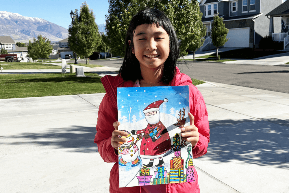 Bella proudly holding her Christmas painting of Santa Claus and a snowman, showcasing her festive artwork.